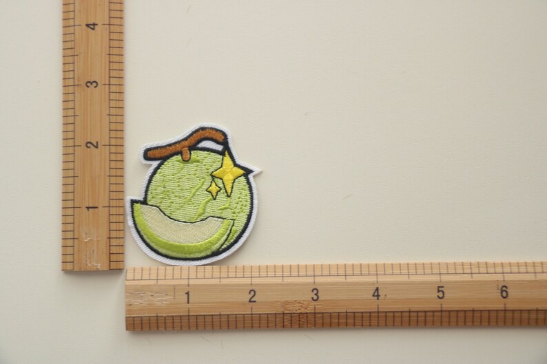 Peut inclure: &Eacute;cusson brod&eacute; repr&eacute;sentant un melon vert avec une tranche coup&eacute;e, une tige marron et deux &eacute;toiles jaunes. L'&eacute;cusson a une bordure blanche, id&eacute;al pour les v&ecirc;tements ou accessoires.