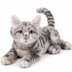 May include: A plush cat toy featuring soft gray fur with darker gray tabby stripes. The stuffed animal has large, alert yellow-green eyes, a small pink nose, and a long, upright tail. It is posed in a lying position with its front paws extended forward.