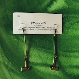 May include: Gold-toned axe earrings with a definition card for the word "propound" on a green background. The card reads: "propound (prǝ-pound') He may propound many ideas, but he can't apply them unless the committee adopts them."