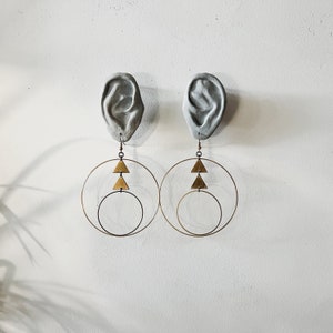 Peut inclure: Une paire de boucles d'oreilles cr&eacute;oles dor&eacute;es avec un motif triangulaire. Les boucles d'oreilles sont suspendues &agrave; un pl&acirc;tre d'oreille.