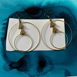 Peut inclure: Une paire de boucles d'oreilles cr&eacute;oles dor&eacute;es avec deux formes triangulaires suspendues &agrave; chaque cr&eacute;ole. Les boucles d'oreilles sont &agrave; double cr&eacute;ole, avec une cr&eacute;ole plus petite &agrave; l'int&eacute;rieur d'une cr&eacute;ole plus grande.