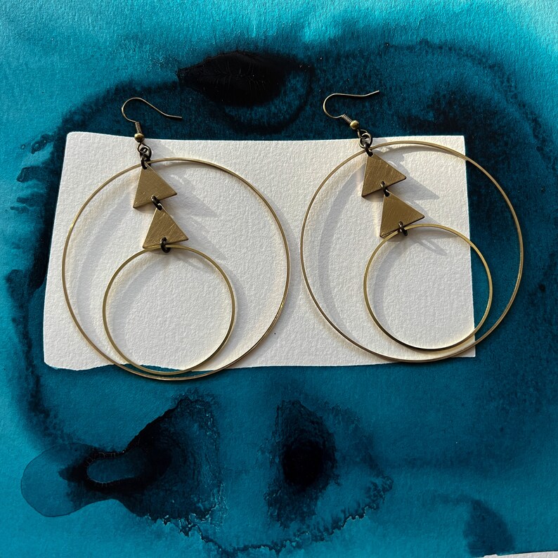 Peut inclure: Une paire de boucles d'oreilles cr&eacute;oles dor&eacute;es avec deux formes triangulaires suspendues &agrave; chaque cr&eacute;ole. Les boucles d'oreilles sont &agrave; double cr&eacute;ole, avec une cr&eacute;ole plus petite &agrave; l'int&eacute;rieur d'une cr&eacute;ole plus grande.