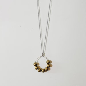 Peut inclure: Un collier en or avec un pendentif rond composé de petites perles dorées. Le collier est sur un fond blanc.