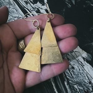 May include: A pair of gold-toned earrings with a triangular shape. Each earring is made of three stacked triangles.