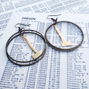 May include: A pair of gold-toned earrings with a double-ring design. Each earring features a gold-colored axe charm hanging from the bottom ring.