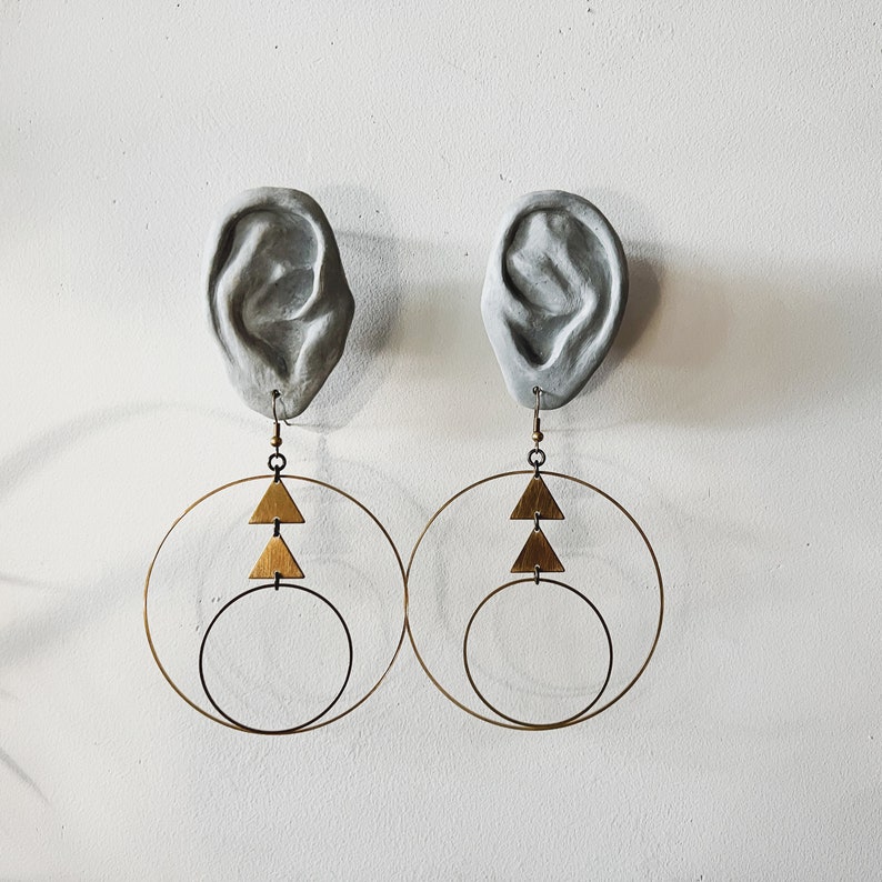 Peut inclure: Une paire de boucles d'oreilles cr&eacute;oles dor&eacute;es avec trois breloques triangulaires suspendues &agrave; chaque cr&eacute;ole. Les boucles d'oreilles sont attach&eacute;es &agrave; des moulages d'oreilles en pl&acirc;tre.