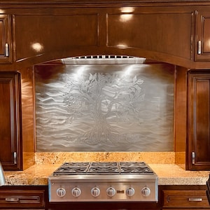 May include: A stainless steel kitchen backsplash with an etched tree design. The backsplash is mounted above a stainless steel gas range with six burners. The kitchen features dark wood cabinetry and a granite countertop.
