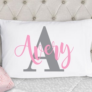 May include: White pillowcase with a gray letter A and the name Avery in pink cursive lettering.