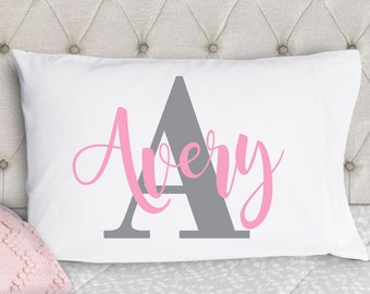 May include: White pillowcase with a gray letter A and the name Avery in pink cursive lettering.