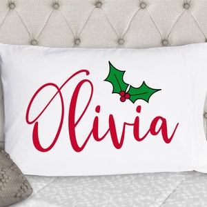 May include: White pillowcase with red cursive text that says "Olivia" and a green holly leaf with red berries.