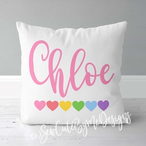 May include: White pillow with the name "Chloe" written in pink cursive lettering.  There are seven rainbow-colored hearts at the bottom of the pillow.