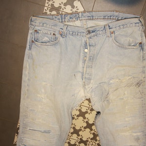 Könnte beinhalten: Hellblaue Jeans aus Denim mit abgenutzten Details und Ausbleichen. Die Jeans haben einen Knopfverschluss und fünf Taschen.