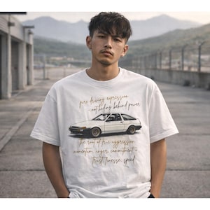 May include: White t-shirt with a car graphic and text. The car is a white coupe. The text reads "pure driving expression - not hiding behind power" and "The root of true aggression: momentum, anger, commitment = trust, finesse, speed."