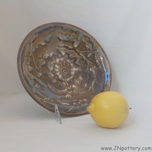 May include: A brown ceramic plate with a swirling, abstract design. The plate has a glossy finish and is decorated with shades of brown, blue, and white.