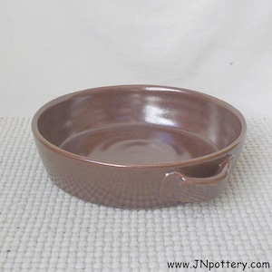 May include: A round, brown ceramic baking dish with two handles. The dish has a textured exterior and a smooth interior. The website address "www.JNpottery.com" is visible at the bottom.