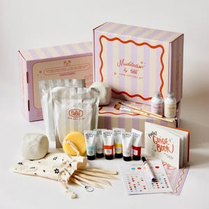 May include: A home pottery kit with boxes, clay, paint tubes, brushes, and a guide book. The boxes are striped with the text "Muditation by PinGit HOME POTTERY KIT". The kit includes air dry clay, paint, and tools.