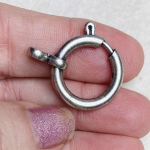 Puede incluir: Cierre de metal plateado con un anillo redondo y un cierre de gancho. El cierre está diseñado para sujetarse a joyas u otros artículos.