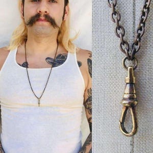 May include: A close-up of a brass chain necklace with a hook clasp. The chain is thick and has a vintage look. The necklace is worn by a person with a white tank top.