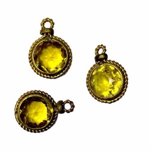 May include: Three gold-toned pendants with yellow glass stones. Each pendant has a rope-like border around the stone.