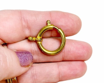 Op de afbeelding: Gouden metalen sluiting met een ronde ring. De sluiting is bedoeld om sieraden of andere voorwerpen aan te bevestigen.