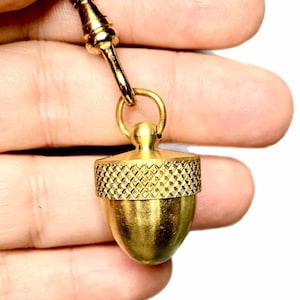 Può includere: Un portachiavi a forma di ghianda di colore dorato con la parte superiore testurizzata e un anello per attaccare le chiavi.