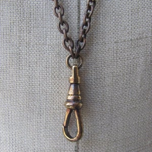 May include: A brass watch chain with a t-bar clasp. The chain is made of linked rings and has a dark brown patina.