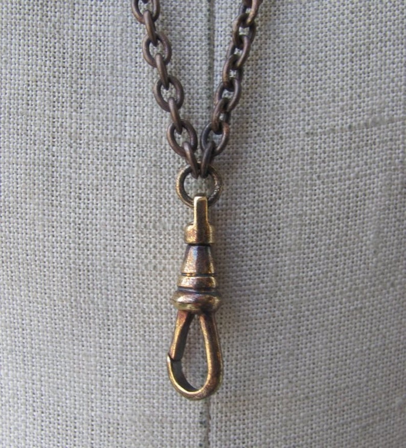 May include: A brass watch chain with a t-bar clasp. The chain is made of linked rings and has a dark brown patina.