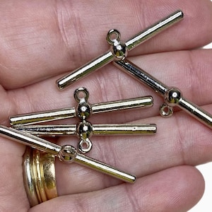 May include: Five silver metal toggle clasps with a round ball at the center of each clasp. The clasps are designed to be used for jewelry making or other craft projects.