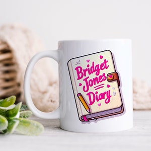 Könnte beinhalten: Weiße Keramiktasse mit einer rosa und weißen Illustration eines geschlossenen Buches mit dem Text "Bridget Jones Diary" auf der Vorderseite.