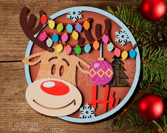 May include: A round, brown wooden sign with a blue border. The sign features a cartoon reindeer with a red nose and a string of colorful lights. The reindeer is holding a purple ornament with a white design. The sign also has a snowflake and the word "Hi" in white.