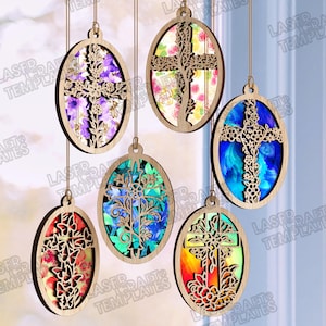 May include: A collection of wooden oval ornaments, each with a laser-cut cross design and a colourful background. The backgrounds display floral or abstract patterns. The ornaments are suspended by strings. The colours include purple, blue, and red.