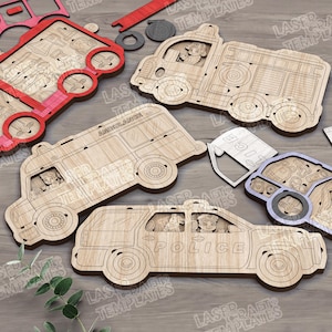 May include: Wooden toy vehicles including a fire truck, ambulance, police car, and a red firetruck puzzle. The vehicles are made of light-colored wood and feature cut-out details. The word "POLICE" is visible on the police car.