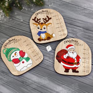 Peut inclure: Des puzzles de Noël Roll-a-Dice en bois avec un renne, un bonhomme de neige et le Père Noël. Chaque puzzle a un design unique avec des sections de lancer de dés. Un dé blanc est également présent.