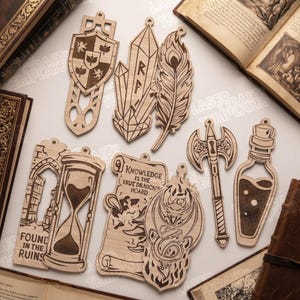 Op de afbeelding: Een verzameling van acht lasergesneden houten bladwijzers met fantasieontwerpen, waaronder een schild, kristallen, een veer, een zandloper met de tekst Found in the Ruins, een perkamentrol met de tekst Knowledge is the True Dragon's Hoard, een draak, een bijl en een flesje.