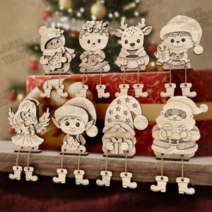 Può includere: Una collezione di ornamenti natalizi in legno con vari personaggi festivi, tra cui un pupazzo di neve, una renna, un elfo e Babbo Natale. Ogni ornamento ha gambe pendenti ed è realizzato in legno chiaro, perfetto per le feste.