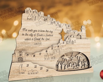 May include: Wooden Christmas advent calendar with laser-cut designs. Features a nativity scene, star, and biblical text. Numbers 1-24 are displayed, with illustrations of buildings and figures. The calendar is made of light-colored wood.