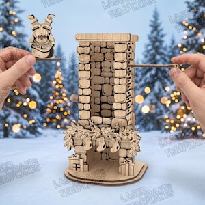 May include: A laser-cut wooden advent calendar shaped like a stone fireplace with a mantle decorated with pine branches and three stockings. A separate wooden cutout of Santa Claus is held to the side, and a small wooden piece with the number 7 is visible.