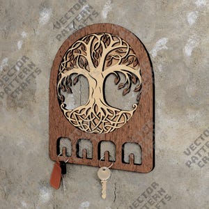 Puede incluir: Porta llaves de madera con un diseño de árbol de la vida. El soporte tiene cinco ganchos para colgar llaves. El árbol de la vida está tallado en madera marrón claro y el soporte es de madera marrón oscuro.