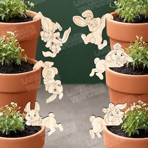 Op de afbeelding: Houten konijnenversieringen in verschillende poses, sommige met bloemendetails, geplaatst rond terracotta bloempotten gevuld met groen. Ideaal voor Pasen of lentedecoraties.