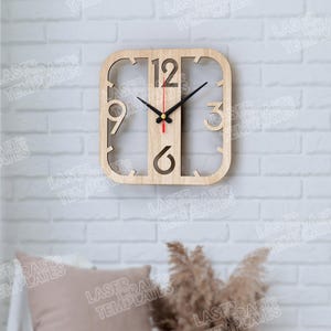 May include: A square wooden wall clock with cut-out numbers 12, 3, 6, and 9. The clock has black hands and a red second hand. The clock is mounted on a white brick wall. The clock's design is minimalist and modern.