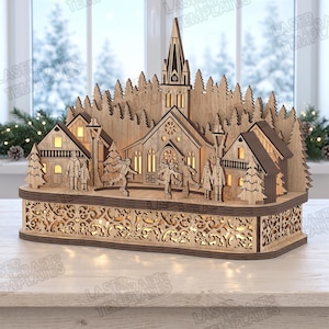 Op de afbeelding: Een lasergesneden houten winterdorp-scène met een centrale kerk met toren, omliggende huizen, dennenbomen en figuren die schaatsen op een ijsbaan. De basis heeft een ingewikkeld filigraanpatroon en interne warme verlichting.
