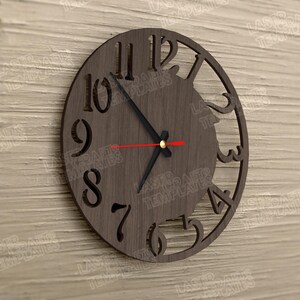 Puede incluir: Un reloj de pared redondo de madera con n&uacute;meros recortados y un dise&ntilde;o decorativo. El reloj tiene manecillas negras y un segundero rojo. El reloj tiene aproximadamente 30 cm de di&aacute;metro.