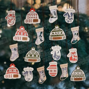 May include: A collection of wooden Christmas ornaments in various shapes, including mittens, hats, and stockings. Each ornament is intricately cut with festive designs and personalized names. They hang from brown strings against a blurred green background.