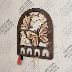 May include: Wooden key holder with a butterfly design. The holder has five hooks and is painted in shades of brown. The butterfly is intricately cut out and has a light brown and dark brown color scheme.