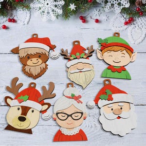 Puede incluir: Adornos navideños de madera con diseños festivos, incluyendo a Papá Noel, un elfo, un reno y una vaca de las Tierras Altas, todos con gorros navideños. Los adornos están pintados con colores brillantes y tienen un lazo para colgar.