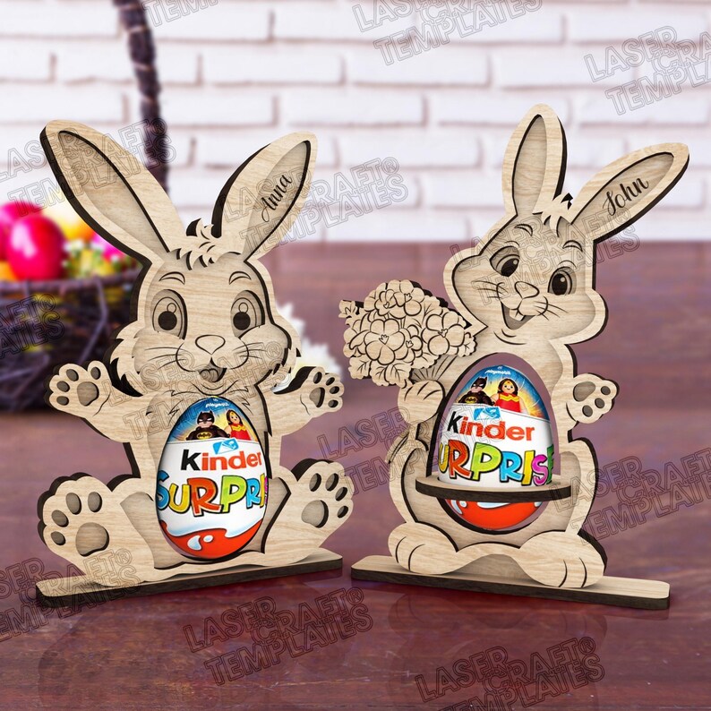 May include: Two wooden Easter bunny decorations. Each bunny holds a Kinder Surprise egg. One bunny has the name "Anna" on its ear, the other has "John". The bunnies are light brown and have a playful design.