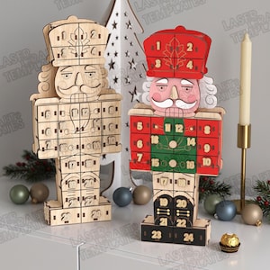 May include: Two wooden nutcracker advent calendars with 24 numbered drawers. One is natural wood, the other is painted red, green, and black. Both feature a soldier design with a tall hat, mustache, and grid-like drawer layout for counting down days.