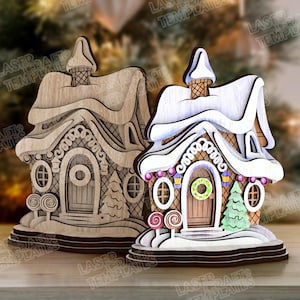 May include: Two wooden gingerbread house decorations. One is unfinished, the other is painted with white snow, colorful candies, and a green wreath on the door. The houses have intricate details and are designed for the holiday season.