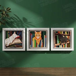 Pode incluir: Três obras de arte de gatos emolduradas. A primeira apresenta um gato branco sobre um livro. A segunda mostra um gato laranja. A terceira retrata um gato preto. Cada gato está situado em um fundo de livros coloridos.