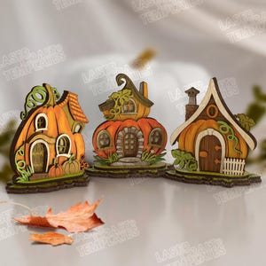 Könnte beinhalten: Drei dekorative Holzhäuser in Kürbisform. Die Häuser sind orange, braun und grün bemalt und weisen detaillierte Elemente wie Türen, Fenster und Schornsteine auf. Ideal für Herbst- oder Halloween-Dekorationen.